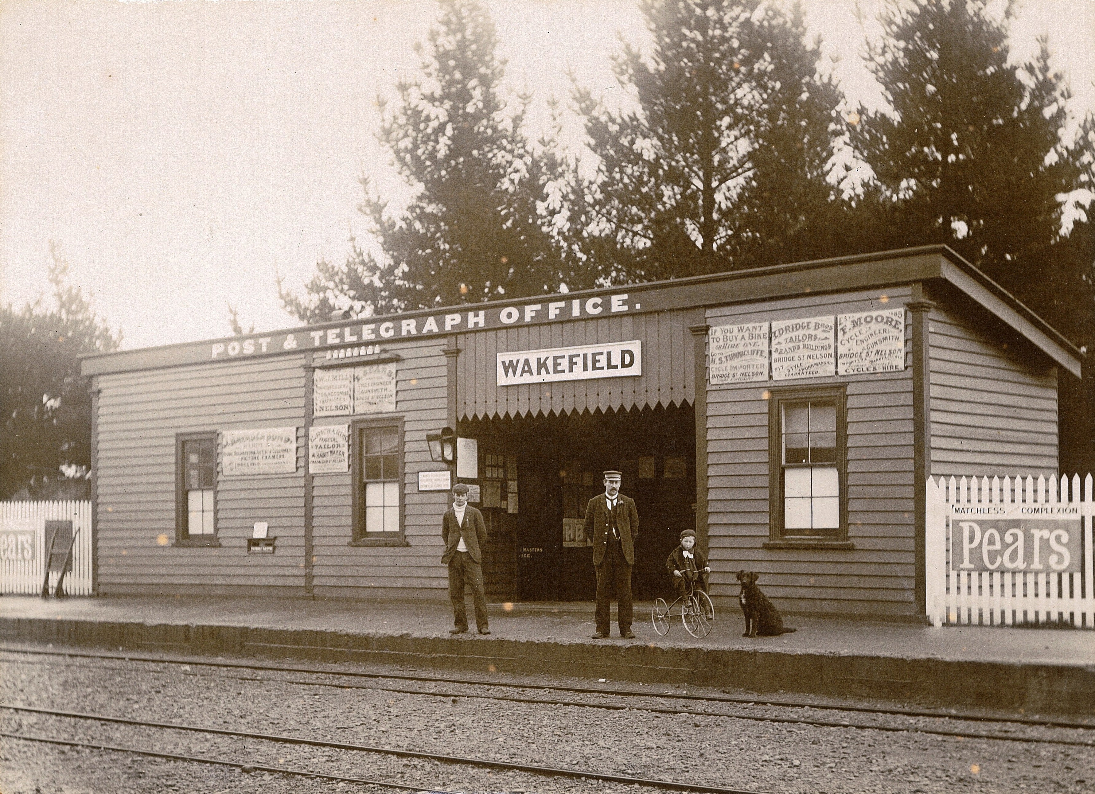 Sepia photograph of station Master William Henry Martin and his son Thomas Stanley Martin (on trike) and Ben the dog, with unnamed assistant, c.1903.